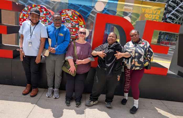  a group of students and teacher in front of a Detroit Sign